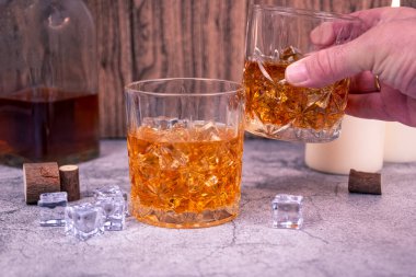 Yükseltilmiş bir viski bardağı, buzda başka bir bardağın üzerinde şişe ve mum ışığıyla şıngırdar. Kutlama ve gece hayatı kavramı, bağımlılık veya alkolizm farkındalığı temaları için de kullanılabilir.