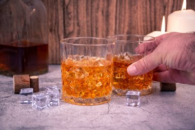 Bir el, buzda başka bir bardağın yanında viski bardağını tutar. Arka planda da mum ve şişe vardır. İçki, alkol kullanımı veya alkolizm farkındalığı paylaşımı için karamsar bar kavramı.