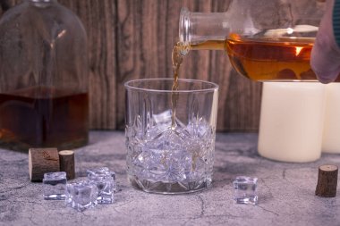 Elle şişeden viskiyi buz küpleriyle dolu kristal bir bardağa boşaltır. Mum ışığında kırsal bir zemine. İçki, alkol tüketimi veya alkolizm bilincine hizmet etme kavramı.