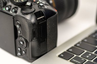 DSLR kamera gövdesinin bir dizüstü bilgisayar klavyesinin yanında yakın plan çekimi, dosya transferi ve dijital düzenleme çalışma akışı kavramı.