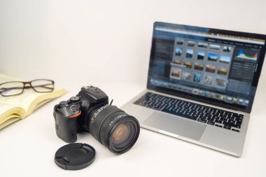 DSLR kamerasıyla fotoğraf düzenleme çalışma alanı, resim galerisini gösteren dizüstü bilgisayar, açık defter ve gözlük, yaratıcı öğrenme ve prodüksiyon sonrası konsept.
