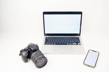 Temiz teknoloji ve fotoğraf seti: boş ekranlı dizüstü bilgisayar, DSLR kamera ve bolca fotokopi alanı olan beyaz arka planda akıllı telefon. Yaratıcı iş akışı, uzaktan çalışma ve pazarlama için ideal.