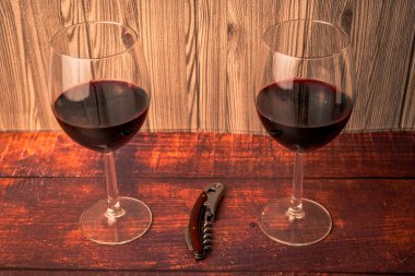 Kırsal ahşap üzerinde tirbuşonu olan iki kadeh kırmızı şarap, sıcak ışık ve ahşap arka plan, akşam yemeği, konukseverlik ve tatma kavramları için mükemmel..