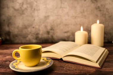 Samimi bir sahne, fincan tabağında kahve fincanı, açık bir kitap ve sade ahşap mumlar. Sıcak akşam havası ve fotokopi alanı.