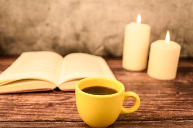 Ön planda açık bir kitapla kahve fincanı ve arka planda hafifçe bulanık mumlar. Fotokopi uzayı ile sıcak bir hayat.