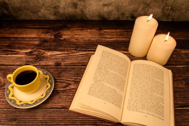 Üst kattaki rahat hayat: açık kitap, kahve fincanı ve kırsal ahşap masada yanan iki mum. Metin için bir sürü kopyalama alanı.