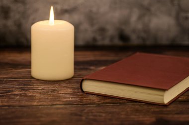 Kırsal bir ahşap masada kapalı kırmızı bir kitabın yanında mum yaktı. Metin ve markalaşma için kopyalama alanı olan minimal konforlu arkaplan.