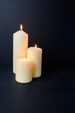 Koyu arka planda sıcak parıltılı üç sütun mum, samimi bir spa ortamı ve kopyalama alanı..