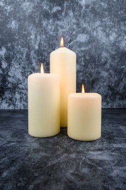 Koyu arkaplanda üç tane beyaz sütun mumu var. Sıcak mum ışığı, rahatlama ve sağIık kavramı.