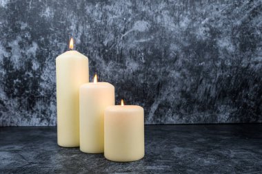 Koyu desenli arka planda, derinlemesine dizilmiş üç sütun mum. Kopya alanı ile asgari sağIık kavramı.