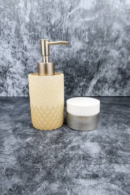 Kozmetik krem kavanozunun yanında koyu renk desenli altın pompalı bej sabun makinesi. Minimum tuvalet cildi modeli..