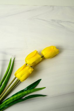 Beyaz mermer zemin üzerinde üç sarı lale ve yeşil yapraklar minimum düz yatar..