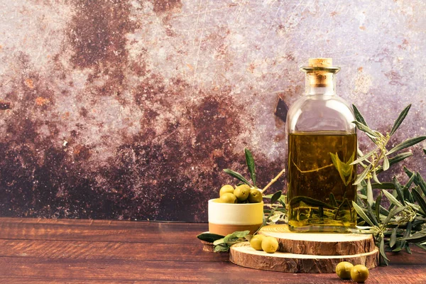 Olive oil bottle with green olives and olive branches on a rustic wooden table with wide copy space.