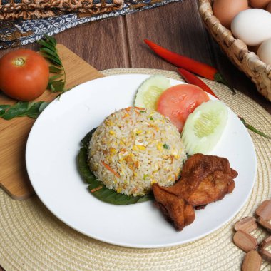 Kızarmış tavukla servis edilen bir tabak pilav, salatalık dilimleri ve geleneksel yemek düzeninde domates garnitürü..