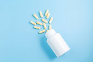 İlaç şişesi ve beyaz haplar açık mavi arka plana dökülmüş. İlaçlar ve reçeteli haplar arka plandaydı.