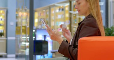 Kadın alışveriş merkezinde otururken kredi kartı ve akıllı telefon kullanıyor. Yüksek kalite fotoğraf