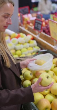 Kadın marketin meyve reyonundan taze sarı elma seçiyor. Yüksek kalite dikey 4k görüntü
