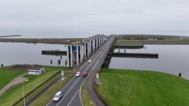 Araçlar, kamyonlar ve araçlar gelgit bariyeri, çimenli setler arasında hareket ediyor.