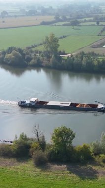 Büyük bir kargo gemisinin güzel bir kırsal bölgede nehir boyunca mal taşıma görüntüsü.