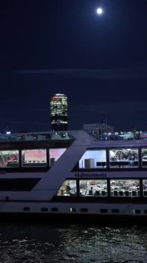 Aydınlatılmış bir turist teknesi. İnsanlar bir nehirde geceleri gökyüzüne doğru yelken açıyorlar.