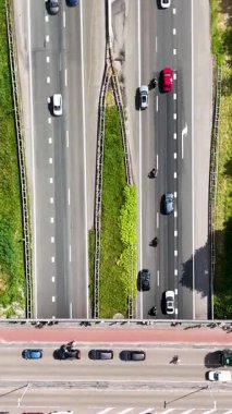 Yüksek açılı insansız hava aracı görüntüleri çok şeritli otoyol ve kavşak boyunca araba ve motosikletleri gösteriyor.