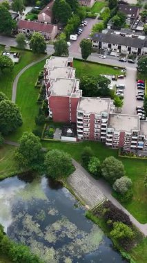 Daireleri, evleri, yeşil parkı ve göleti olan bir yerleşim yerinin tepeden aşağı görüntüsü.