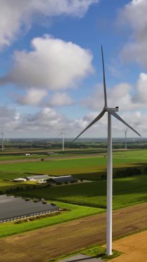 Güneşli bir günde tarım arazisi üzerinde temiz ve yenilenebilir enerji üreten bir rüzgar türbininin hava görüntüsü