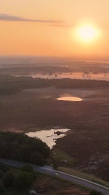 Altın saatinde sisli bir kırsal alanda seyahat eden yalnız bir aracın hava görüntüsü.