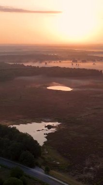 Gökyüzü perspektifi güzel bir altın gün doğumu sırasında gölleri ve ormanları olan sisli bir manzarayı gösteriyor.