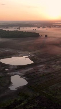 Sabah güneşi, göller ve ormanlarla kaplı sisli bir araziyi aydınlatarak çarpıcı bir hava manzarası sağlar.