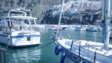 Mavi çamurluklar, yansıtıcı su, liman etkinliği ve hafif sallanma ile yan yana demirlenmiş yatlar.