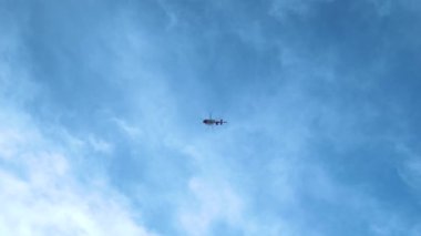 Acil tıbbi servis helikopteri bulutlu mavi gökyüzünde ağır çekimde uçuyor.