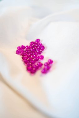 Pembe şeffaf kapsüller ya da pembe boncuklar beyaza saçılmış.