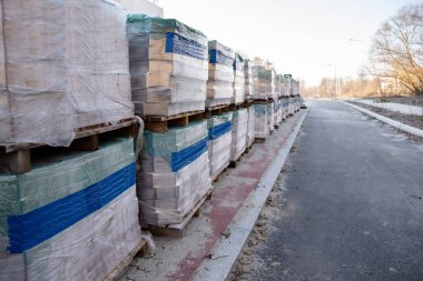 İnşaat alanındaki paletlerin üzerine paketlenmiş yapı malzemesi yığını