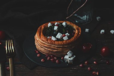 Lezzetli bir restoran menüsünde çeşitli hamur işleri vol-au-vent aperatifleri, kremalı tavuk, sığır eti ve ıspanaklı feta karışımı, koyu seramik tabaklarda kaplanmış ve gıda fotoğrafçılığı için taze garnitürlerle süslenmiş.