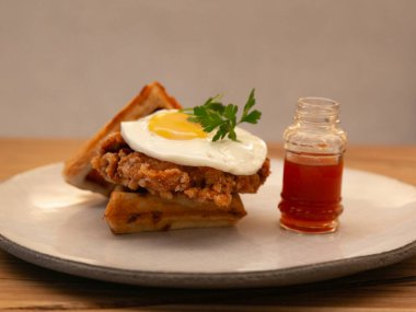 Kızarmış tavuk ve waffle, üstünde sahanda yumurta, beyaz tabakta servis edilmiş restoran brunch fotoğrafçılığı ahşap bir masada, ön manzara.