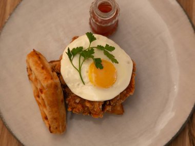 Kızarmış tavuk ve waffle, üstünde sahanda yumurta, beyaz tabakta servis edilmiş restoran brunch fotoğrafçılığı ahşap bir masada, ön manzara.