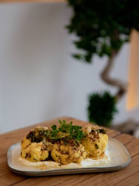 Kremalı karnabahar yoğurt sosu ve otlarla ısırır, restoran aperatifi fotoğrafçılığı, tahta masa üzerindeki dikdörtgen tabakta ön manzara.