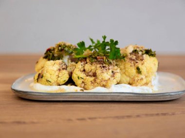 Kremalı karnabahar yoğurt sosu ve otlarla ısırır, restoran aperatifi fotoğrafçılığı, tahta masa üzerindeki dikdörtgen tabakta ön manzara.