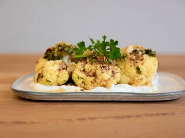 Kremalı karnabahar yoğurt sosu ve otlarla ısırır, restoran aperatifi fotoğrafçılığı, tahta masa üzerindeki dikdörtgen tabakta ön manzara.