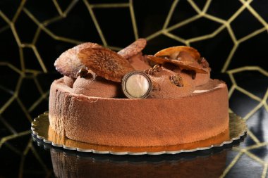 Yuvarlak çikolatalı kremalı pasta borulu girdaplarla süslenmiş, profesyonel fırın gösterisi için altın bir tahtada sunuluyor..