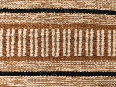 Yatay bantlı kaba örülmüş tekstil ve toprak tonlarında dikey çizgiler, zanaatkarlığı yansıtıyor..