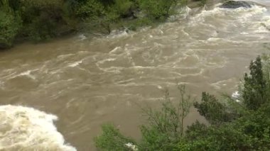 Şiddetli yağmurun ardından hızlı ve çalkantılı nehir akışı. Şiddetli yağış sonrasında akıntının hızını ve türbülansını artıran güçlü bir su dalgası nehrin aşağısına hücum eder. Kabarık akıntı güç ile çalkalanır ve beyaz köpük oluşturur.