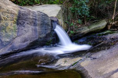 Orman deresindeki granit kayaların üzerinde çağlayan küçük bir şelalenin manzarası. Su, uzun pozlama fotoğraf teknikleri nedeniyle ipeksi ve pürüzsüz görünüyor. Konsept rahatlama, saflık ve hareket iletir. Otantik gerçek fotoğrafçılık.