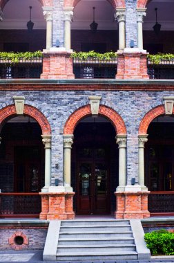 Klasik kemerli koridorlar, beyaz sütunlar ve balkon içeren klasik kırmızı ve gri tuğla bir binanın mimari ayrıntıları. Tarzı 20. yüzyıl başları sömürge ya da Shikumen mimarisini işaret ediyor. Otantik gerçek fotoğrafçılık.