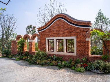 Kıvrımlı çatısı ve peyzaj bahçesinde açık pencereleri olan zarif kırmızı tuğlalı mimari yapı. Görüntü kültürel mirası ve klasik tasarımı aktarıyor. Yüksek kaliteli gerçek fotoğrafçılık..