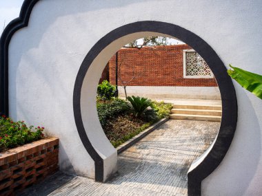 Beyaz bir duvarın içindeki klasik dairesel ay kapısı girişi bir bahçe yoluna çıkıyor. Görüntü gizemi, Zen felsefesini ve doğu mimari güzelliğini aktarıyor. Yüksek kaliteli gerçek fotoğrafçılık..