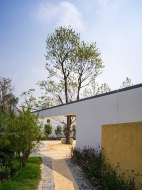 Beyaz bir duvar, gri kiremitli çatı ve yeşil bir ağaç içeren modern Çin tarzı bahçe girişinin dikey görüntüsü. Görüntü mimari zarafeti ve zen sadeliğini aktarıyor. Yüksek kaliteli gerçek fotoğrafçılık..