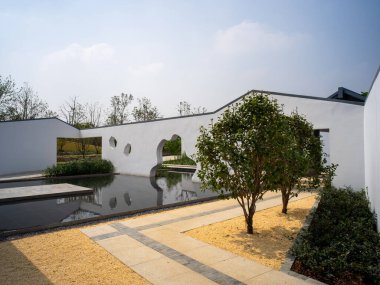 Yansıma havuzu, açıkları ve çakıl yollarıyla beyaz duvarları olan manzaralı bir Çin bahçesinin manzarası. Görüntü armoni, feng shui ve mimari güzelliği yansıtıyor. Yüksek kaliteli gerçek fotoğrafçılık..
