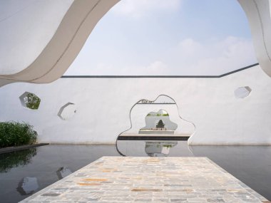 Beyaz bir duvardaki düzensiz bir kemerden yansıma havuzuna ve bahçeye bakıyor. Görüntü derinlik, çerçeve ve geleneksel doğu estetiğini yansıtıyor. Yüksek kaliteli gerçek fotoğrafçılık..